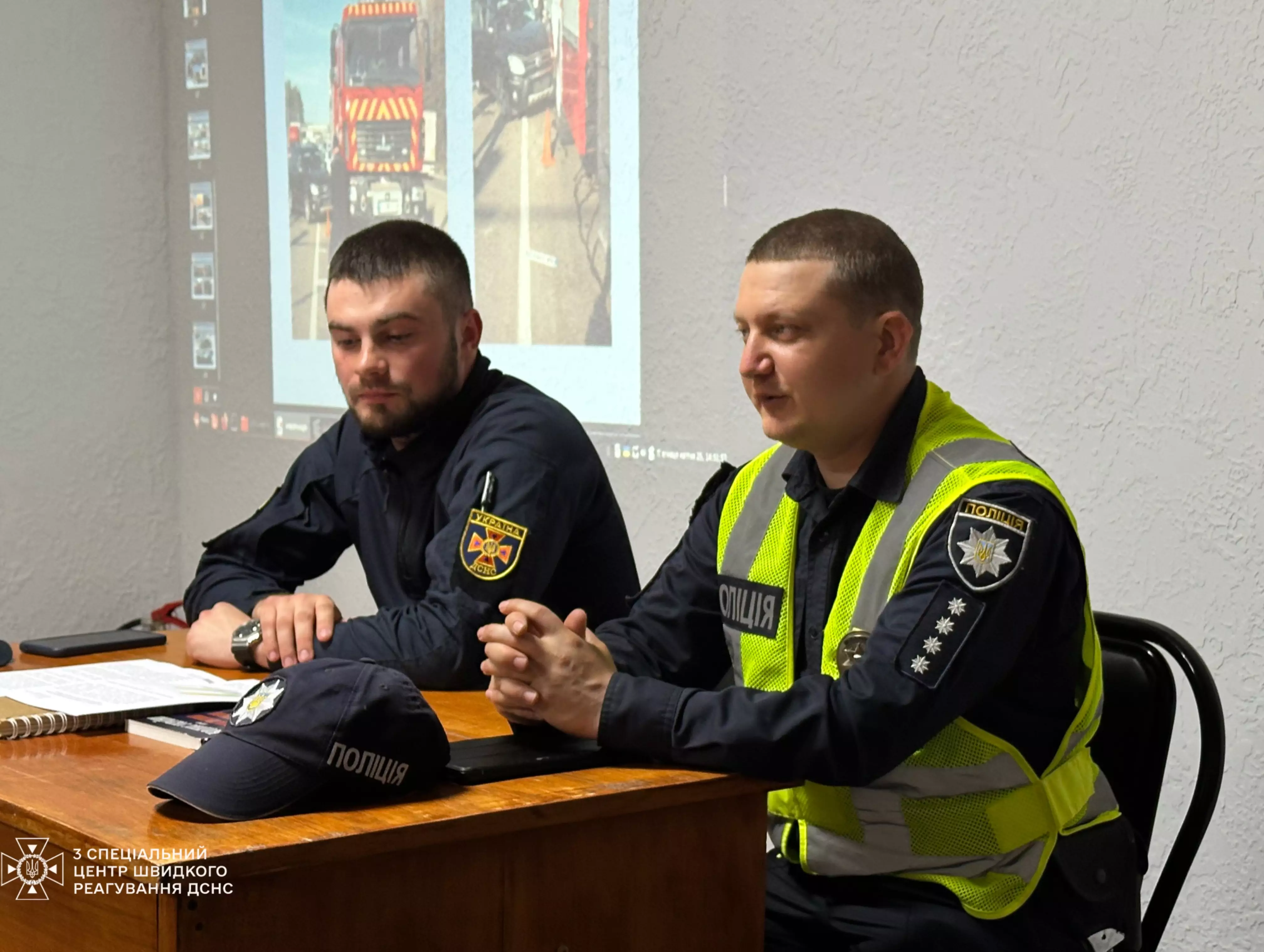 На фото представник поліції та начальник служби безпеки дорожнього руху проводять заняття для водіїв
