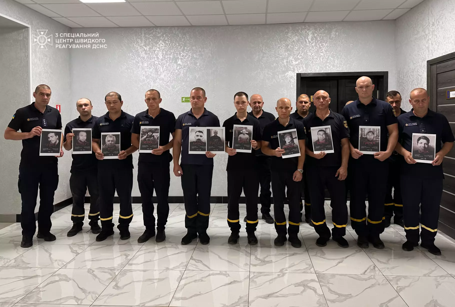 На фото зображені рятувальники, які тримають в руках портрети загиблих Захисників у колонії Оленівкиі 