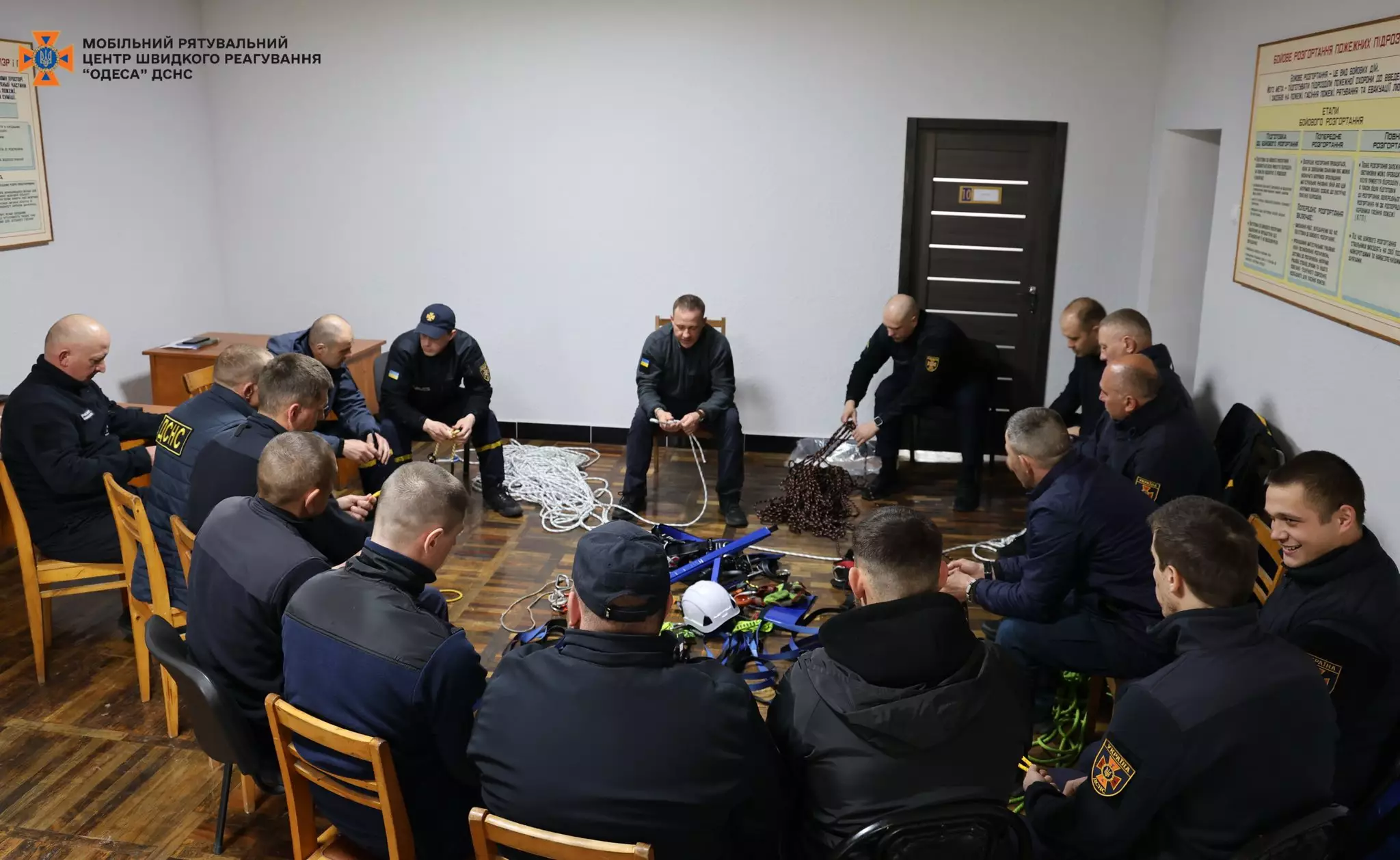 На фото зображені рятувальники та викладач, які сидять колом та слухають викладача