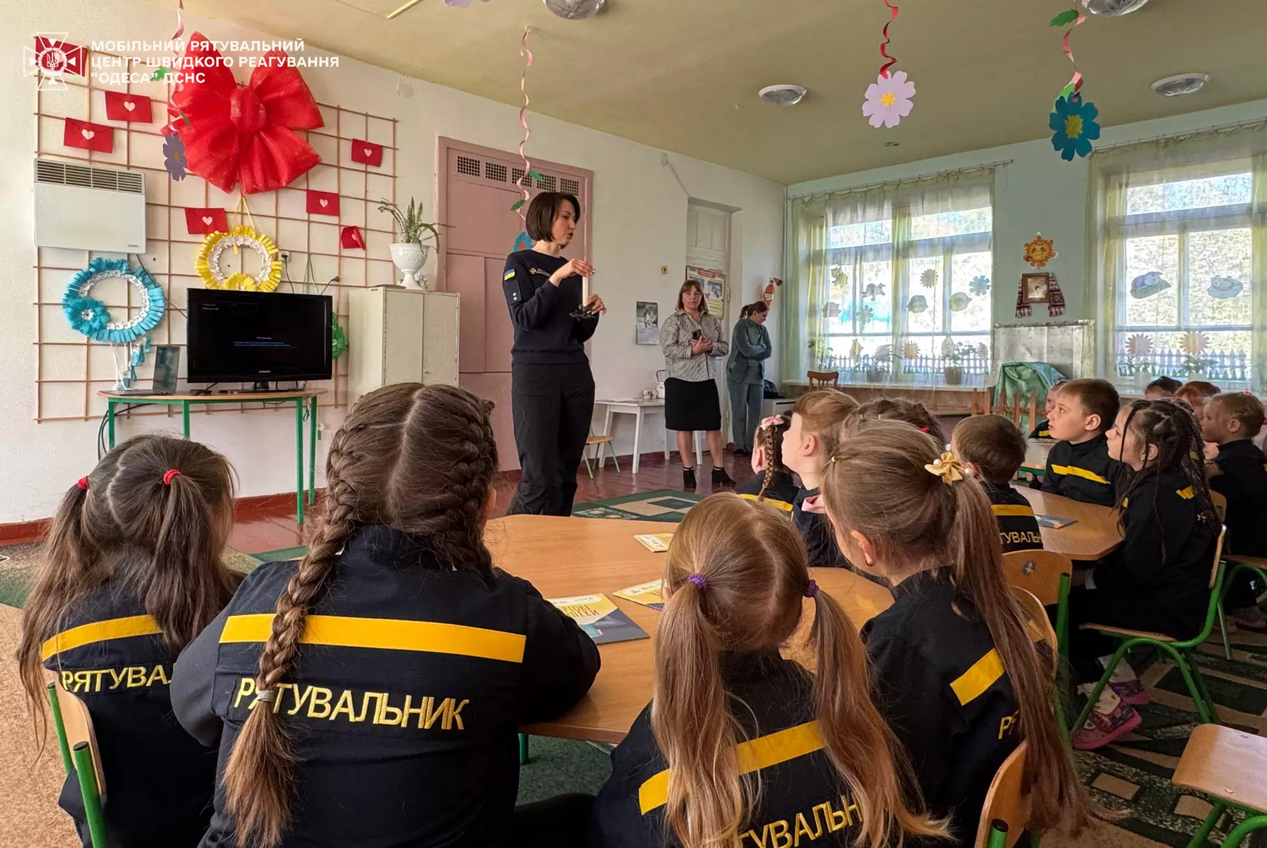 На фото рятувальниця показує дітям свічку, діти сидять за столами
