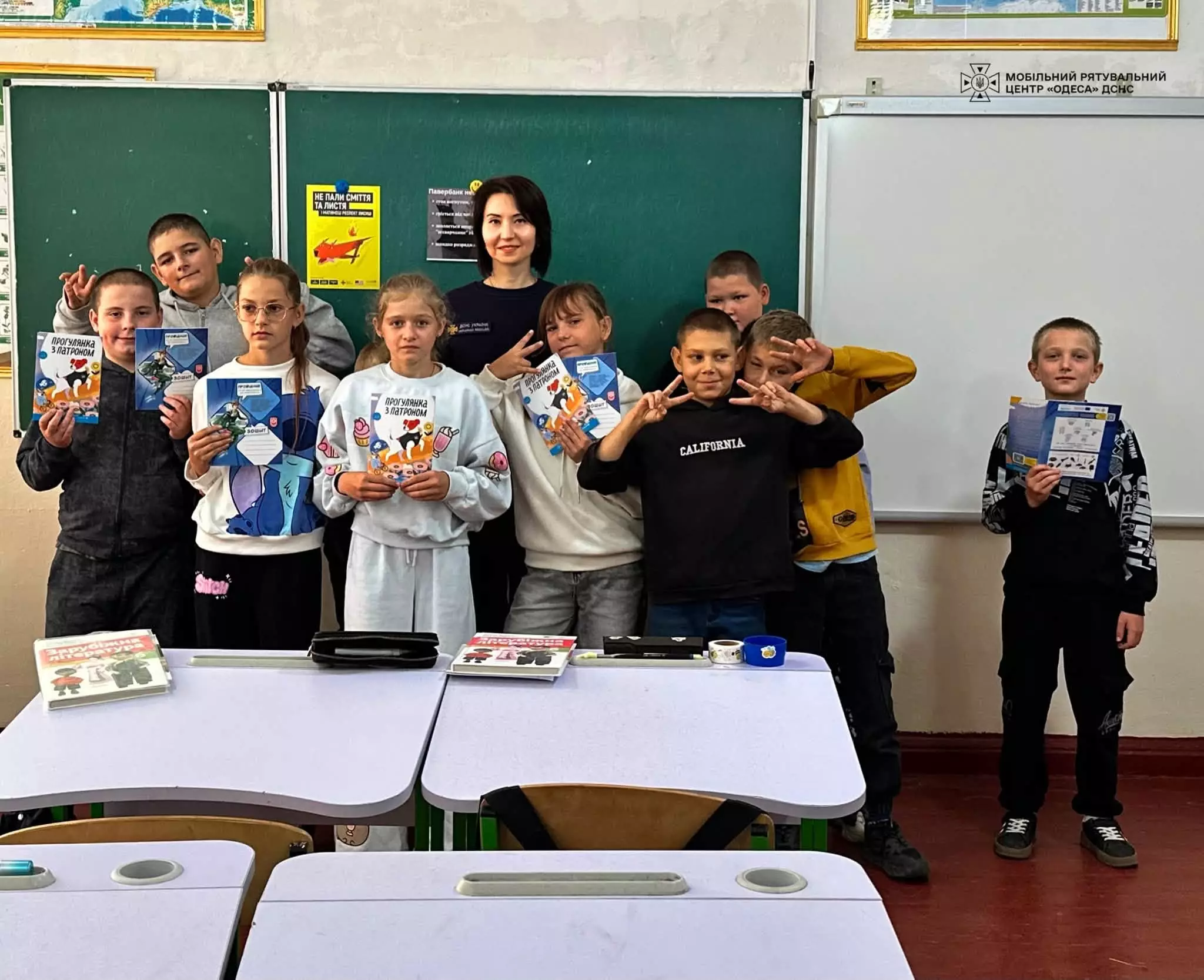 На фото діти разом з рятувальницею і тримають подаровані зошити і книжки 